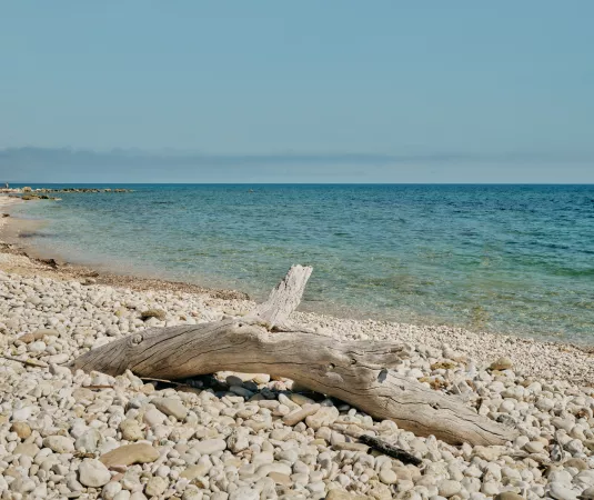The image depicts a tranquil beach scene with a shoreline covered entirely in smooth, round white pebbles
