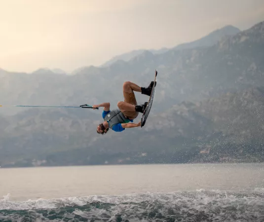 A man flips above the sea while wakeboarding