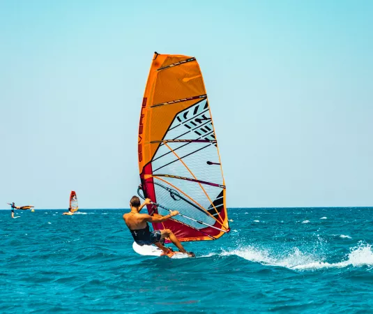 a person windsurfing on a clear, blue sea under a bright sky.