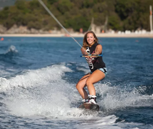 A woman wakeboarding, crossing her wake on a calm sea