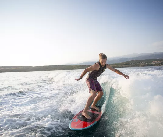 a young man wakesurfing on a red and blue surfboard in the ocean