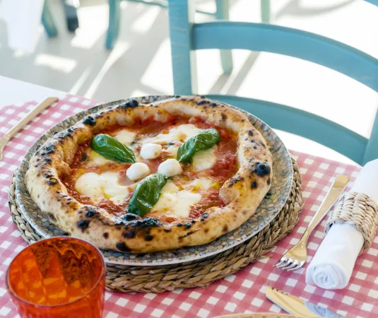 howcases a delicious Margherita pizza placed on a woven charger plate atop a red-and-white checkered tablecloth. 