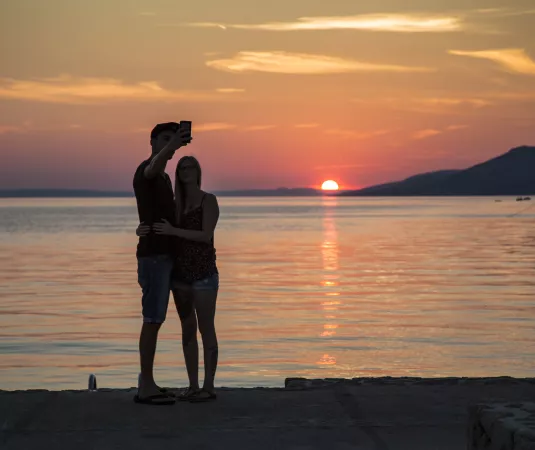 A couple take a selfie in front of a beautiful sunset at Alana beach club