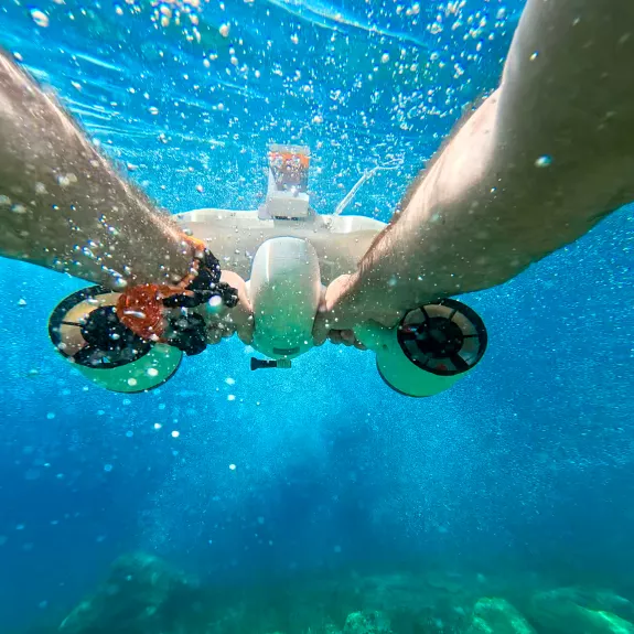 an underwater view of a person holding onto a small, white underwater scooter 