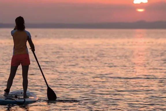 Two women stand up paddle boarding at sunset