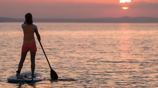 Two women stand up paddle boarding at sunset