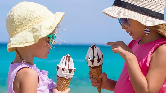 Two young girls eating ice cream on a beach in Italy