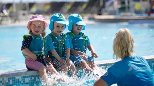 Three young children splashing in pool with nanny