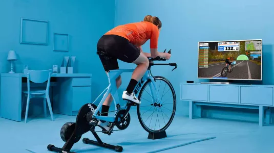 Man in living room and a static bike joining a Zwift ride