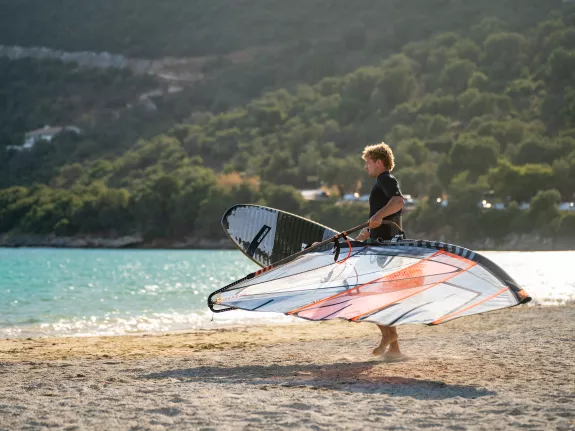 man carrying windsurf kit on the beach
