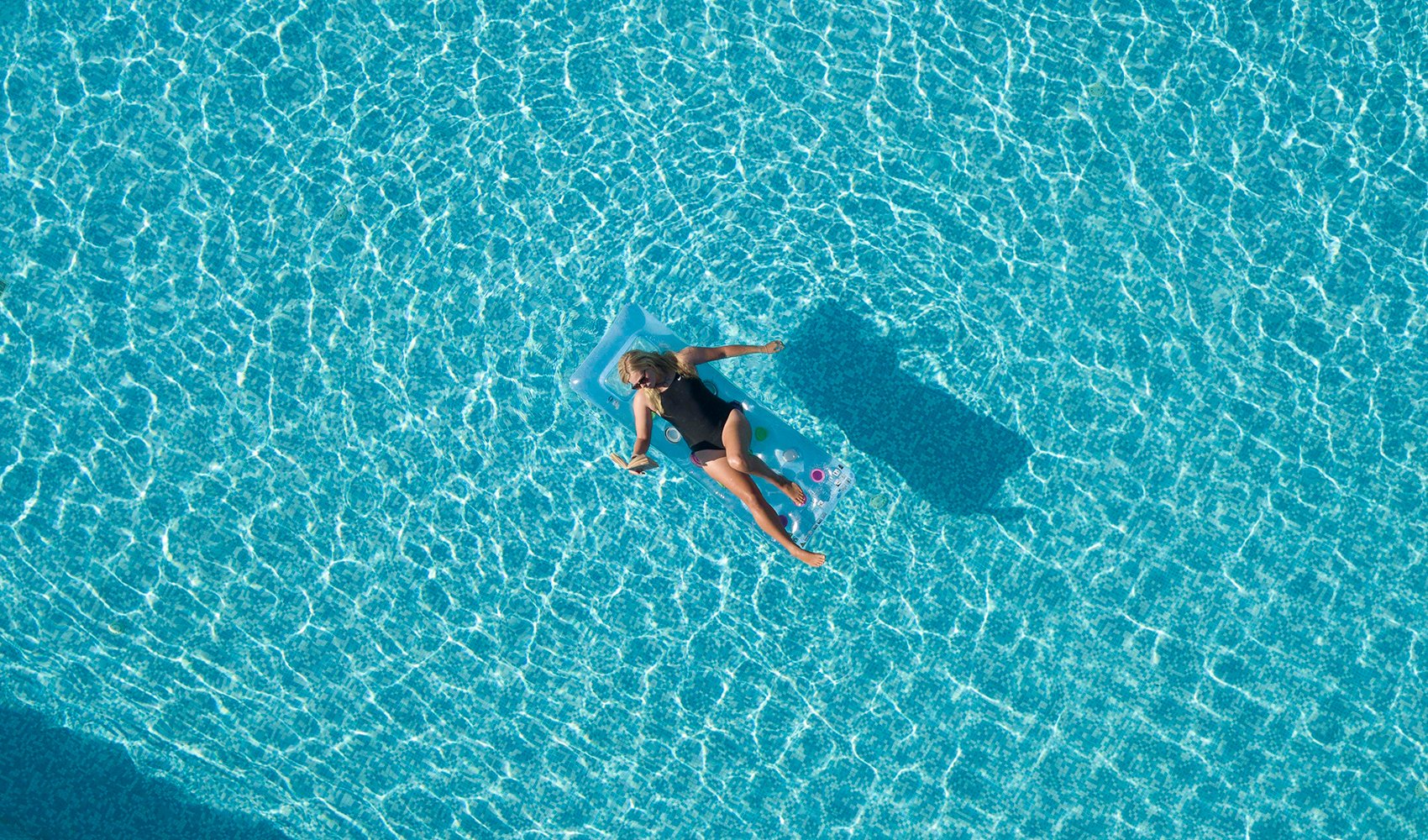 woman reading book while sunbathing in pool